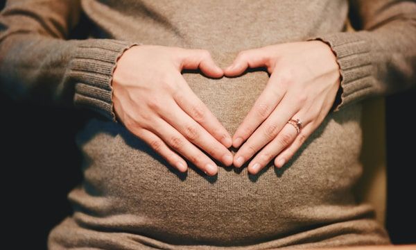 Heart-shaped hands cradling a pregnant belly